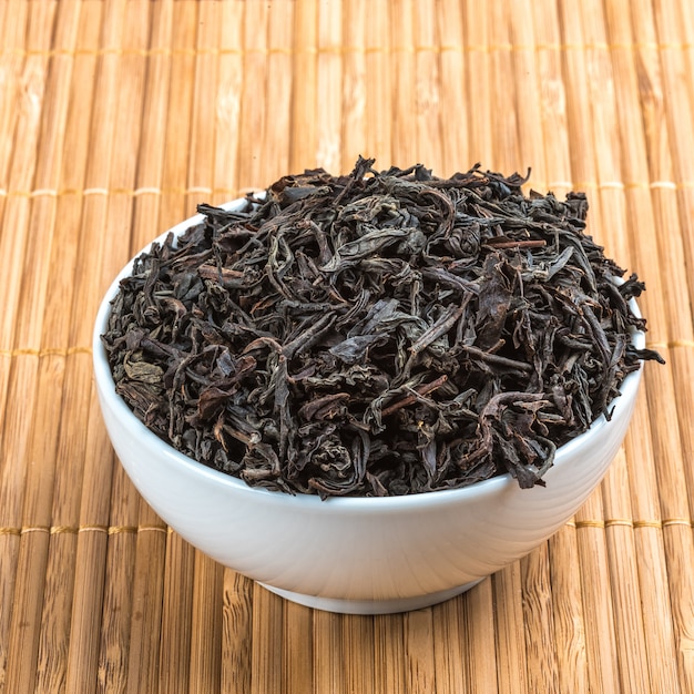 Dried tea is poured into a ceramic cup on a bamboo mat