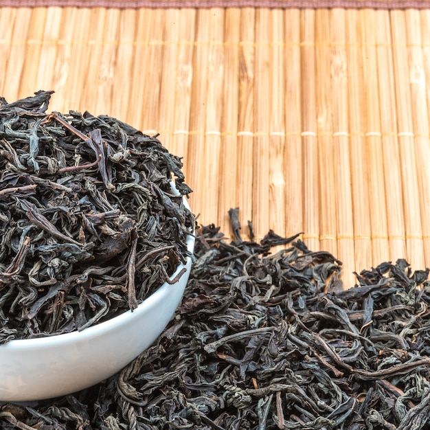 Dried tea is poured into a ceramic cup on a bamboo mat.