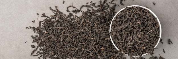 Dried tea is poured into a white ceramic cup on a gray textured background. View from above. Layout.