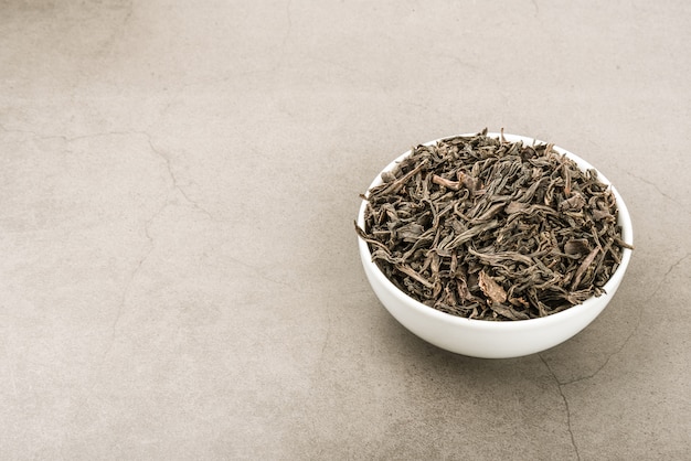 Dried tea is poured into a white ceramic cup on a gray textured