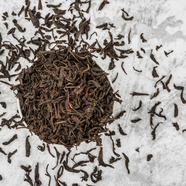 Dried tea is poured into a white ceramic cup on a marble table. View from above. Layout.