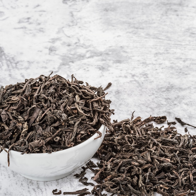 Dried tea is poured into a white ceramic cup on a marble table.