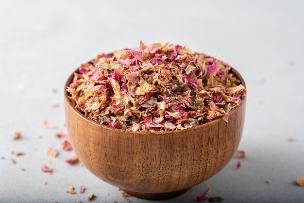 Dried tea rose petals in a wooden bowl.