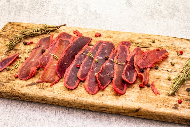 Dried tenderloin of beef meat with dry rosemary and pepper mix on vintage wooden board