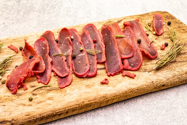 Dried tenderloin of beef meat with dry rosemary and pepper mix on vintage wooden board