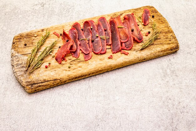 Photo dried tenderloin of beef meat with dry rosemary and pepper mix on vintage wooden board