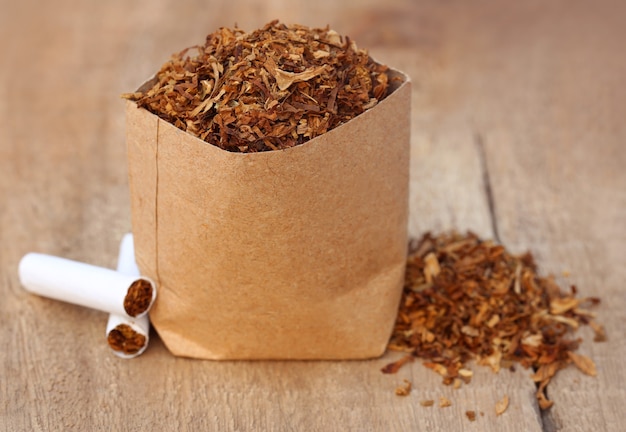 Dried tobacco leaves with cigarette on wooden surface