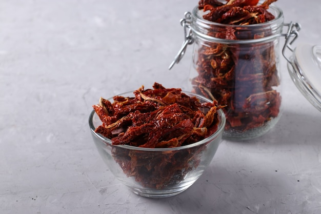 Dried tomatoes in bowl and glass jar on a light gray background. Horizontal format. Closeup