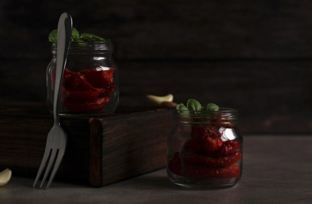 Dried tomatoes in a glass jar with garlic and basil with a fork on a dark background