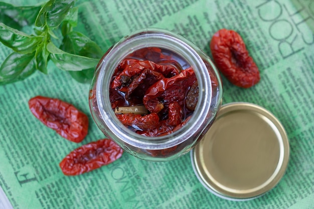 Dried tomatoes in a jar surrounded by ingredients and basil for cooking Rustic style top view