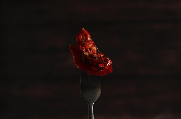 Photo dried tomatoes with italian herbs on a fork on a dark background