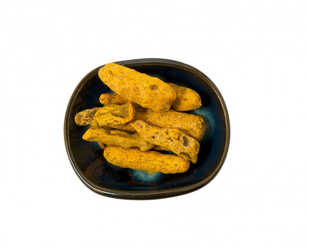 Dried turmeric root in a bowl on a white background. 