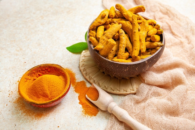 Dried turmeric roots and powder with leaves on a light background.