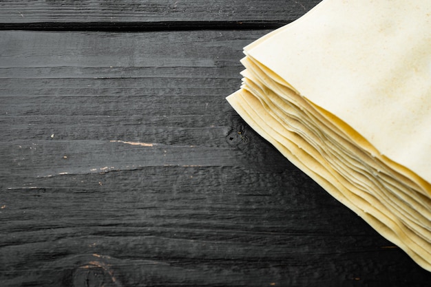 Set di fogli di pasta lasagna cruda secchi, sul tavolo di legno nero