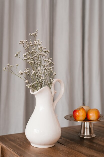 Dried white flowers in a white vase and apples on a wooden table