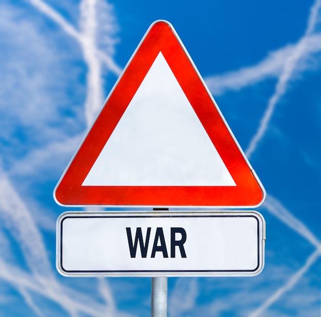Driehoekig verkeerswaarschuwingsbord met het woord - Oorlog - tegen een blauwe lucht doorkruist door meerdere witte contrails van vliegtuigen conceptueel van een gevecht tussen vijandelijke vliegtuigen of luchtafweerraketten.