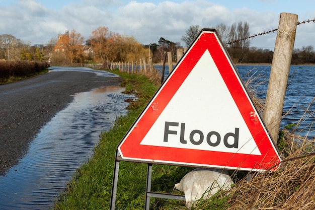 Foto driehoekig waarschuwingsbord voor overstromingen op een weg die is overstroomd door een rivier die is gebroken