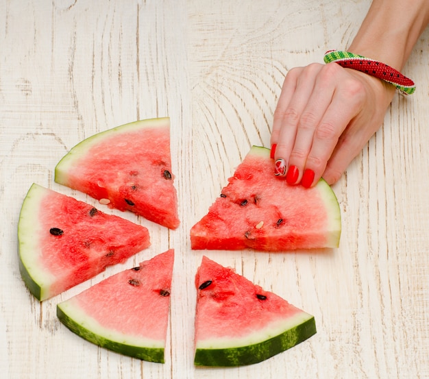 Driehoekige stukjes watermeloen en handen van de vrouw met een manicure op een lichte houten