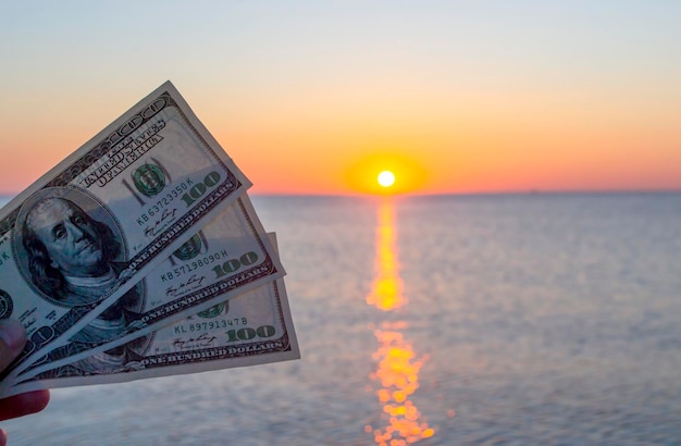 Driehonderd dollarbiljetten op de achtergrond van het zeeoppervlak bij zonsondergang dageraad