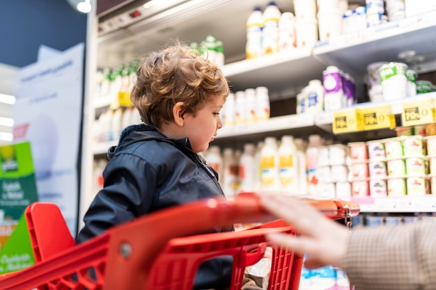 Driejarige jongen in de supermarkt kijkt naar de zuivelproducten uit de kar die kiest