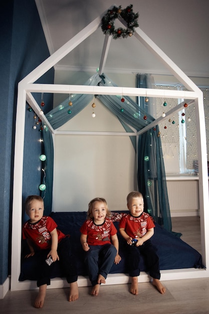 Drieling zittend op het bed versierd voor Kerstmis drie schattige kleine kinderen in rode tshirts