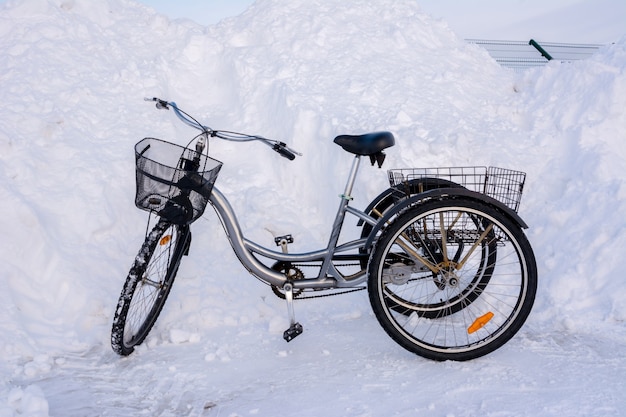 Driewielige fiets in de winter op een achtergrond van besneeuwde heuvels, sneeuwbanken, hekken en asfalt.