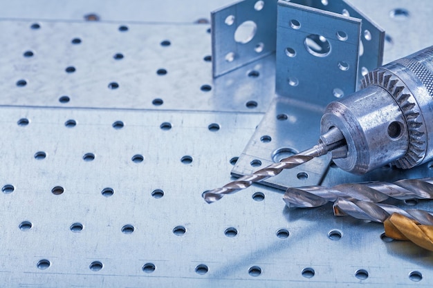 Photo drill with boring bits and angle bars on perforated metallic background construction concept