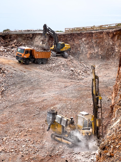 写真 トラックに岩石を積み込む掘削機の隣にある採石場で掘削装置が岩石を掘削する