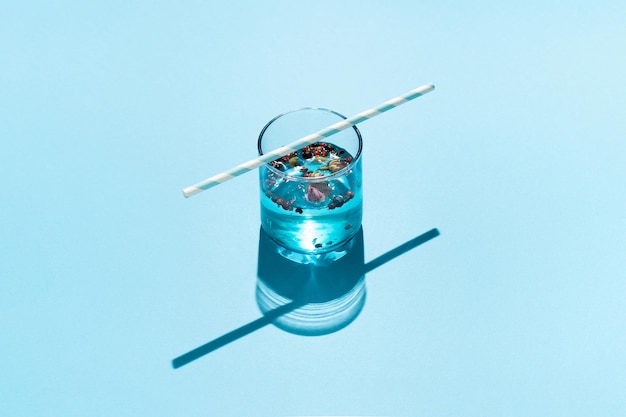 Drink in blue glass with dried roses red peppers and striped paper straw on blue background