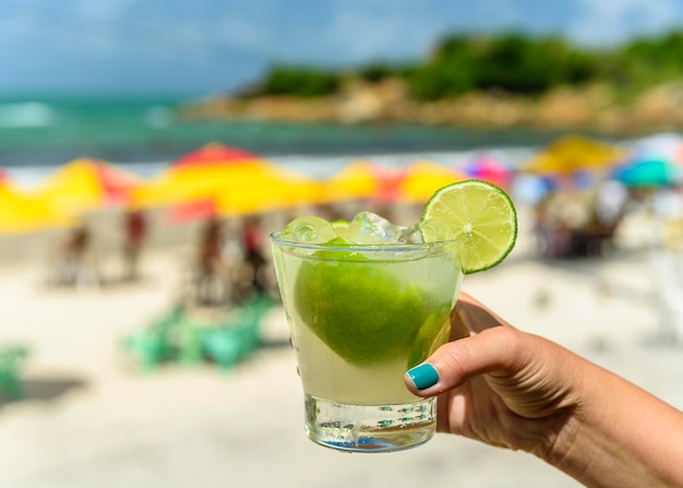 ぼやけた背景とブラジルのビーチでカイピリーニャドリンクを持ってカイピリーニャを飲む