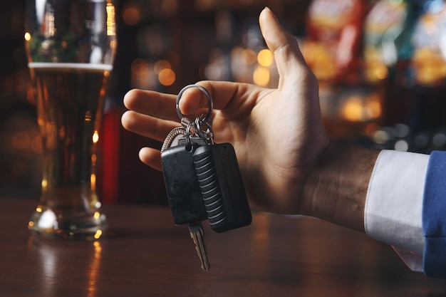 A person's hand holding keys near a tall glass of beer at a bar, suggesting they may drink and drive on Blackout Wednesday.