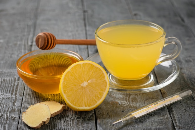 Пейте корень имбиря, лимон, апельсин, мед и корицу и термометр на черном деревянном столе.