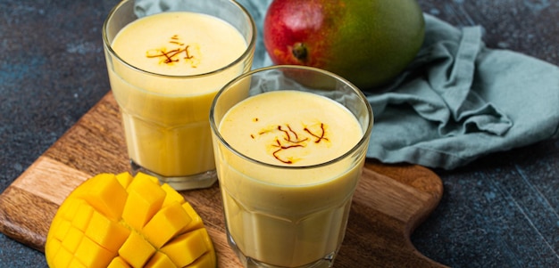 Drink mango lassi in two glasses on rustic concrete table with fresh ripe cut manfo from above