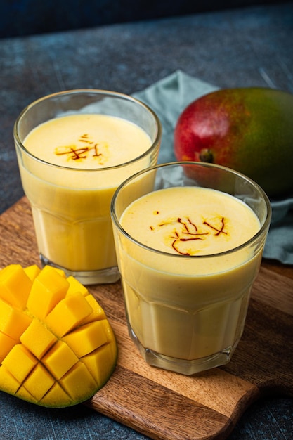 Drink mango lassi in two glasses on rustic concrete table with fresh ripe cut manfo from above