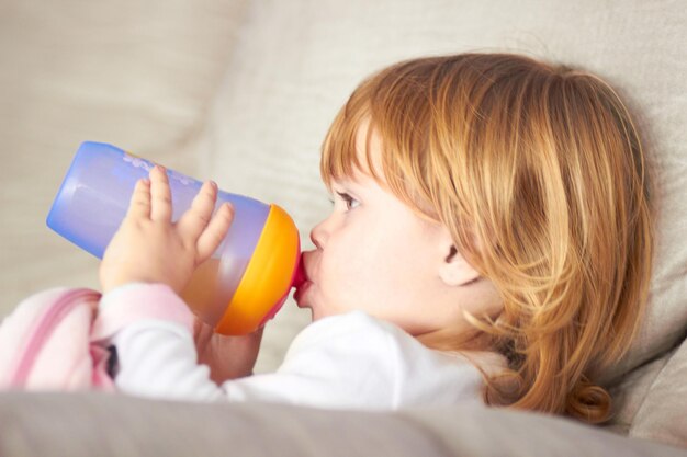 ベビーマグから飲んでいる愛らしい少女のショットを飲みます