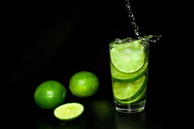 Drink with ice and fresh ripe green limes on black