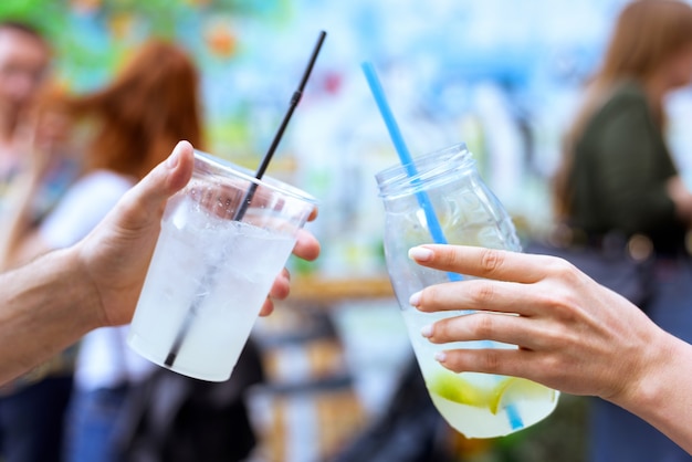 Drinken limonade cocktail glazen met stro en ijs schudden, man en vrouw vriend handen cheers op een evenement met wazig rode haar mensen en gekleurde muur achtergrond