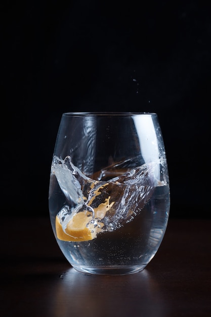 Drinking carbonated water movement drops lemon citrus into a clear glass splashes fly blurred