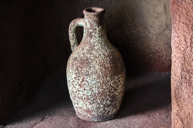 Кувшин глиняный для питья на каменной полке в помещении.