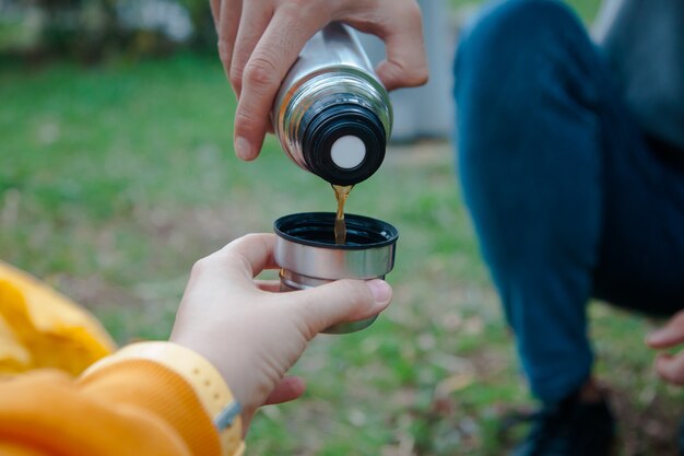 公園でフィルターコーヒーを飲む。魔法瓶からカップにコーヒーを注ぐ。コーヒーの愛の概念。キャンプのコンセプト。