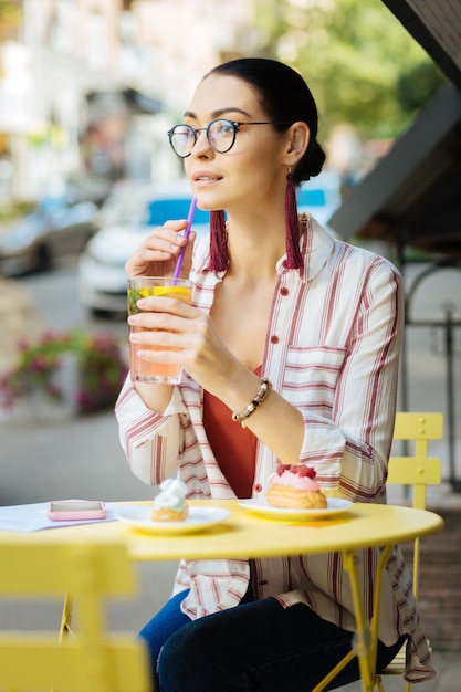 レモネードを飲む。夏のカフェテラスに座って、レモネードを飲みながら思慮深く遠くを見ている美しい若い女性