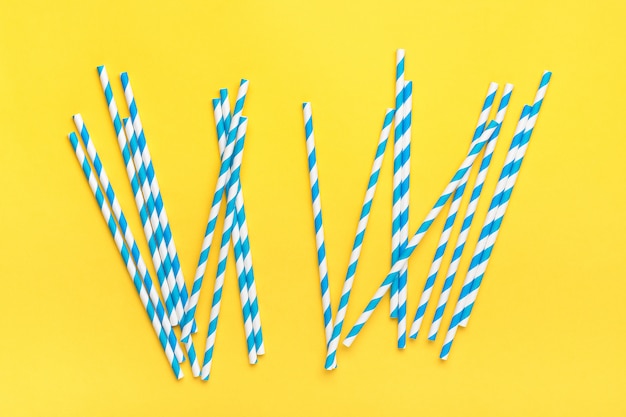 Drinking paper straws for party with blue stripes, ice cube on yellow background with copy space