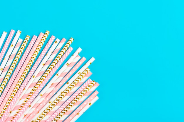 Drinking paper straws for party with golden, white, pastel pink stripes on blue background