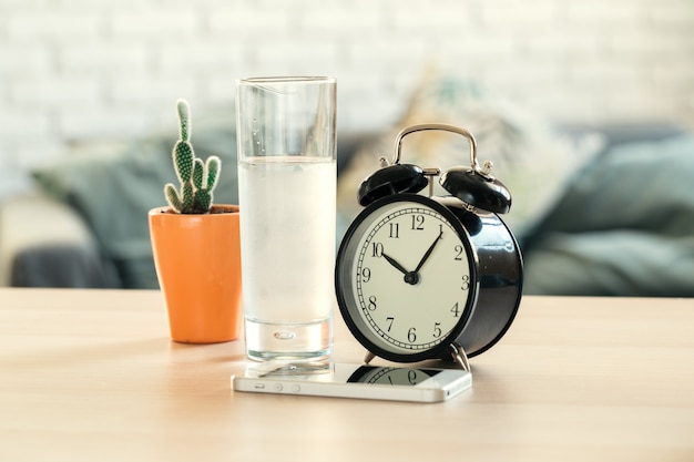 Drinking water health concept. alarm clock and glass of water on table