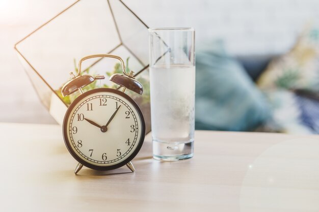 飲料水の健康概念。目覚まし時計とテーブルの上の水のグラス