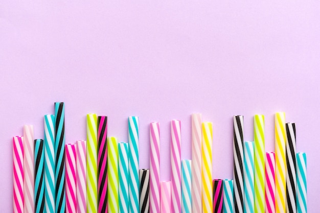 Drinkrietjes met strepen voor feest op lila achtergrond. Bovenaanzicht van kleurrijke plastic buizen voor zomercocktails. Plat liggen