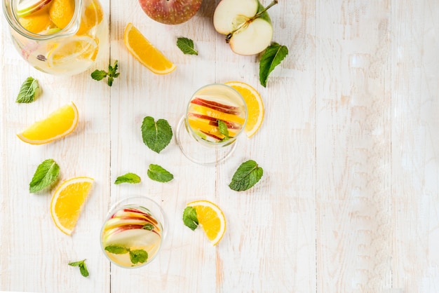 Drinks and cocktails. White autumn sangria with apples, orange, mint and white wine. In glasses for champagne, in a pitcher, on a white wooden table. Copy space top view