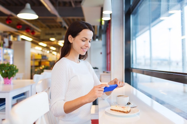 Foto bevande, cibo, persone, tecnologia e concetto di stile di vita - giovane donna sorridente che scatta foto con lo smartphone e beve caffè al bar