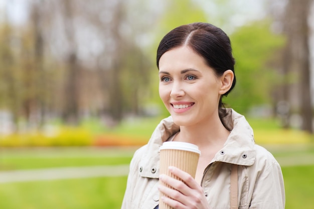 ドリンク、レジャー、人のコンセプト – 公園でコーヒーを飲む笑顔の女性