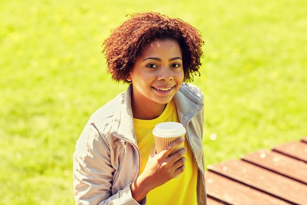 drinks and people concept - smiling african american young woman or teenage girl drinking coffee from paper cup outdoors